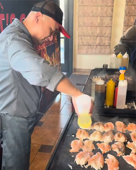 Professional hibachi chef cooking fresh steak, shrimp, vegetables, and fried rice on a hot grill